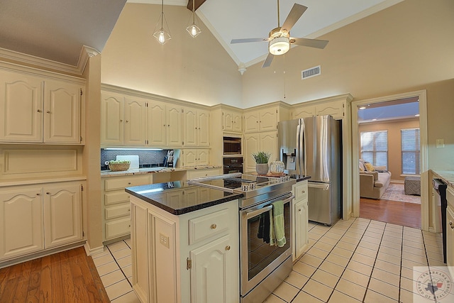 kitchen featuring cream cabinetry, backsplash, a center island, high vaulted ceiling, and black appliances