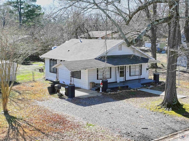 view of front of property featuring gravel driveway, a shingled roof, fence, and a porch