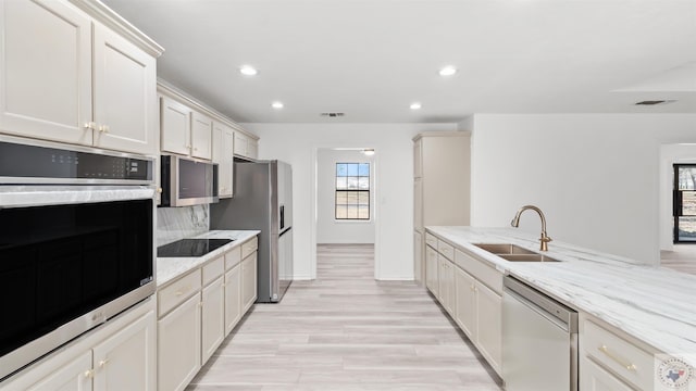 kitchen featuring recessed lighting, light wood-style flooring, appliances with stainless steel finishes, a sink, and light stone countertops