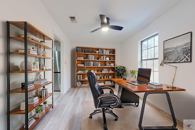 home office with light wood-type flooring, ceiling fan, and visible vents