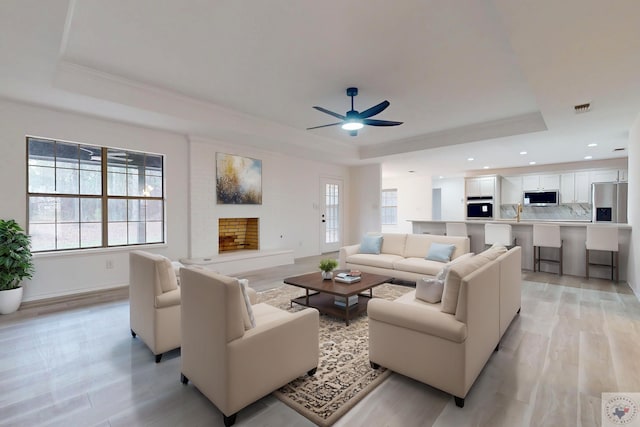 living room with light wood-type flooring, a tray ceiling, visible vents, and a fireplace with raised hearth