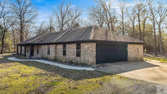 view of side of home featuring a garage, concrete driveway, brick siding, and roof with shingles