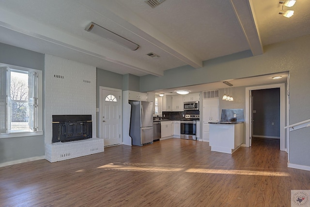 kitchen with appliances with stainless steel finishes, pendant lighting, beamed ceiling, white cabinetry, and tasteful backsplash