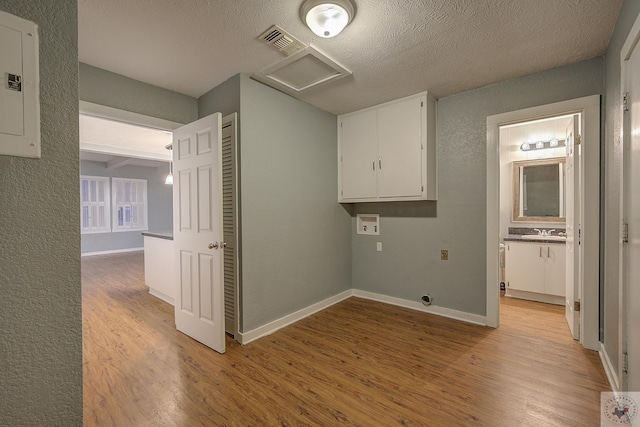 laundry area with sink, hookup for a washing machine, electric panel, light hardwood / wood-style floors, and a textured ceiling