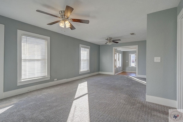 carpeted empty room with ceiling fan, a textured ceiling, and a wealth of natural light