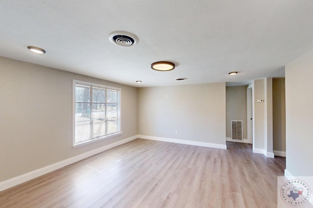 unfurnished room featuring visible vents, light wood-style flooring, baseboards, and a textured ceiling