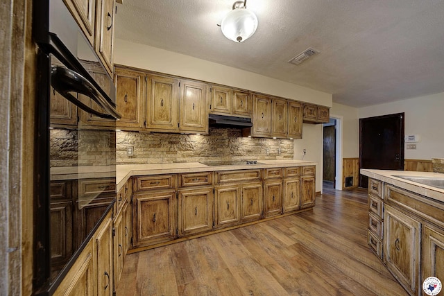 kitchen with black electric cooktop, wainscoting, wood finished floors, light countertops, and under cabinet range hood