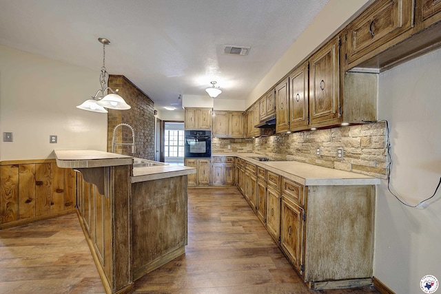 kitchen featuring wood finished floors, visible vents, a sink, black appliances, and a peninsula