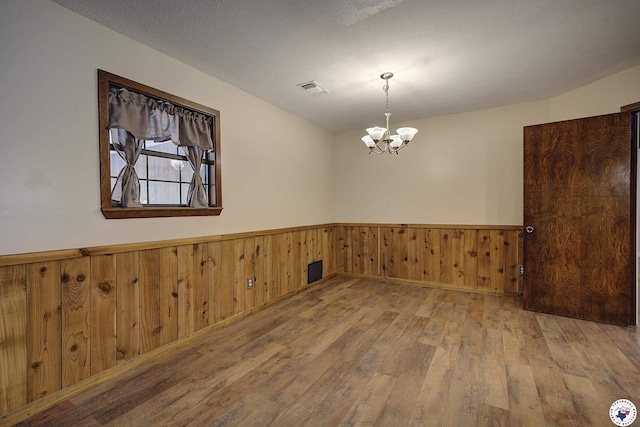 empty room featuring a wainscoted wall, visible vents, a chandelier, and wood-type flooring
