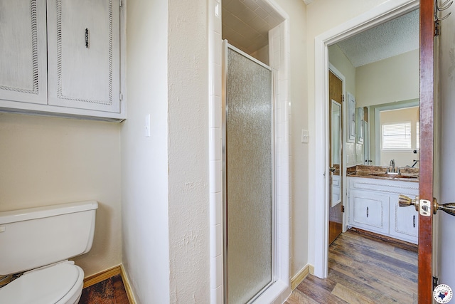 full bath featuring toilet, wood finished floors, a stall shower, vanity, and baseboards