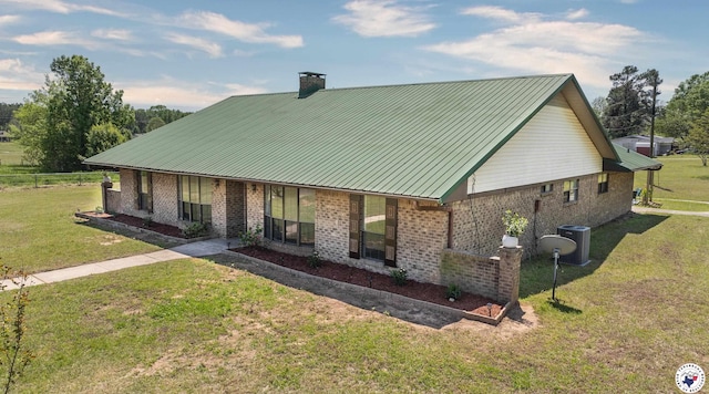 rear view of property with a chimney, central air condition unit, a lawn, brick siding, and metal roof