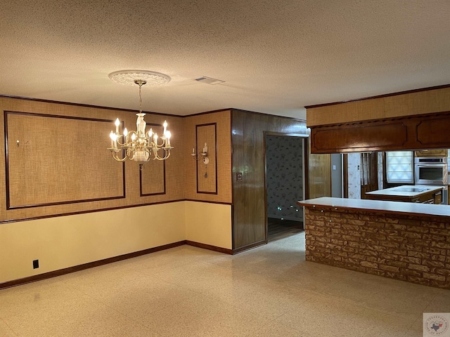 unfurnished dining area featuring wooden walls, an inviting chandelier, a textured ceiling, and ornamental molding