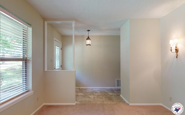 spare room with a textured ceiling, baseboards, light colored carpet, and visible vents