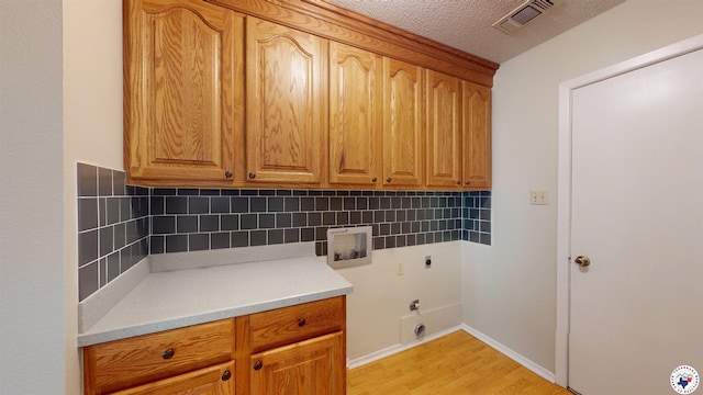 laundry area with cabinet space, light wood finished floors, hookup for a washing machine, electric dryer hookup, and visible vents