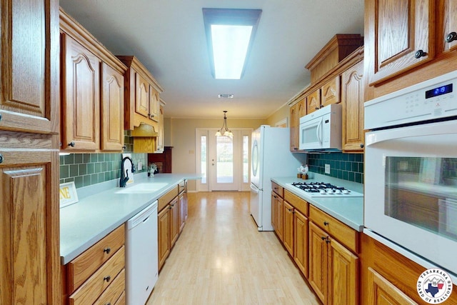 kitchen featuring decorative backsplash, white appliances, light countertops, a sink, and light wood finished floors