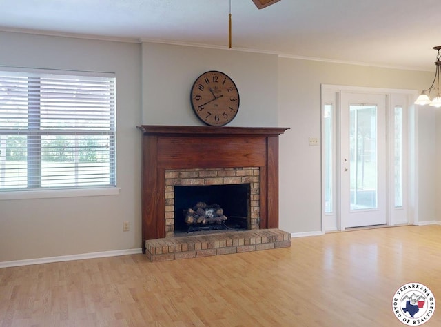 unfurnished living room featuring crown molding, an inviting chandelier, a brick fireplace, wood finished floors, and baseboards