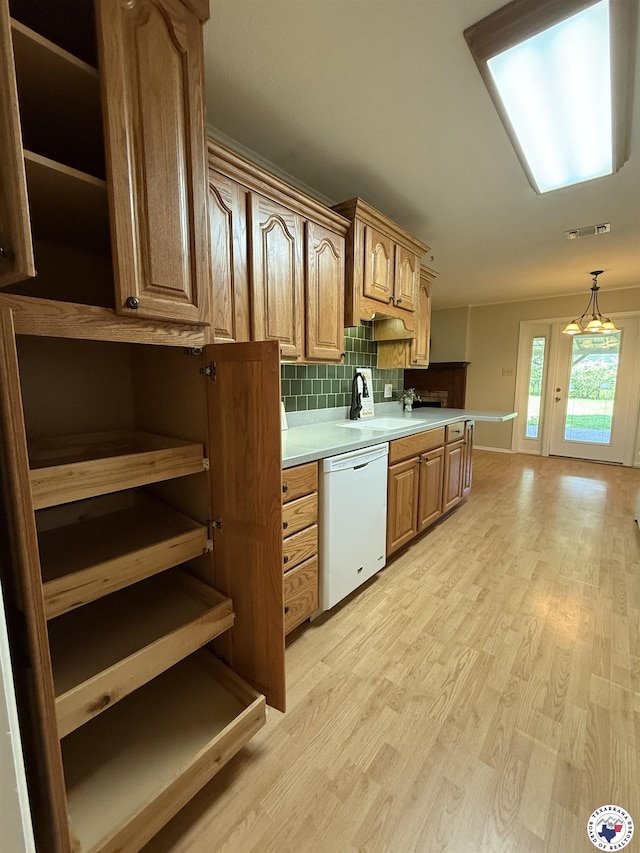 kitchen featuring open shelves, light countertops, a sink, light wood finished floors, and dishwasher