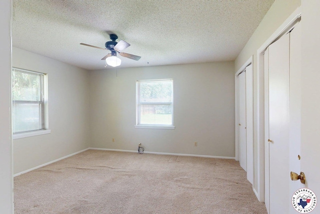 unfurnished bedroom featuring baseboards, a textured ceiling, light carpet, and multiple windows