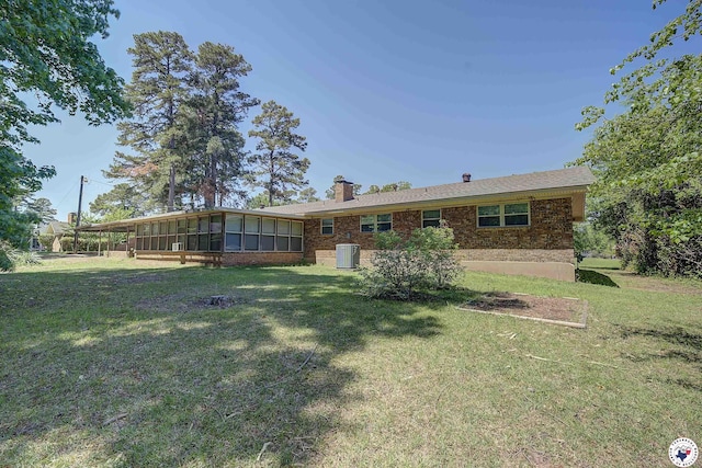rear view of property with a sunroom, a chimney, brick siding, and central AC unit