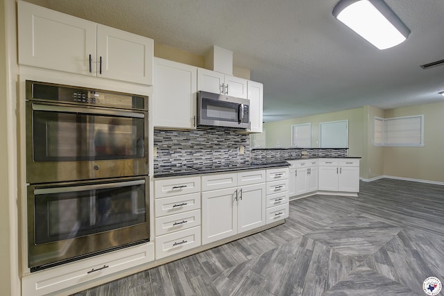 kitchen with a textured ceiling, dark countertops, stainless steel appliances, and a peninsula