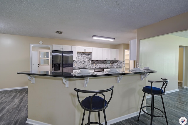 kitchen with dark wood-style flooring, dark countertops, and stainless steel fridge