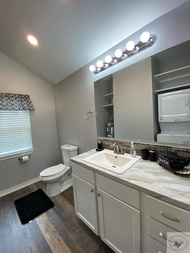 bathroom with hardwood / wood-style floors, toilet, stacked washer and clothes dryer, and vanity