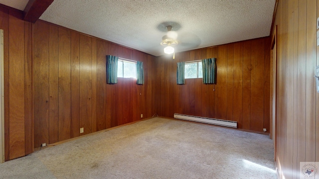 carpeted empty room featuring wood walls, a baseboard heating unit, and a textured ceiling