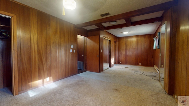 interior space with wooden walls, a textured ceiling, light colored carpet, and beam ceiling