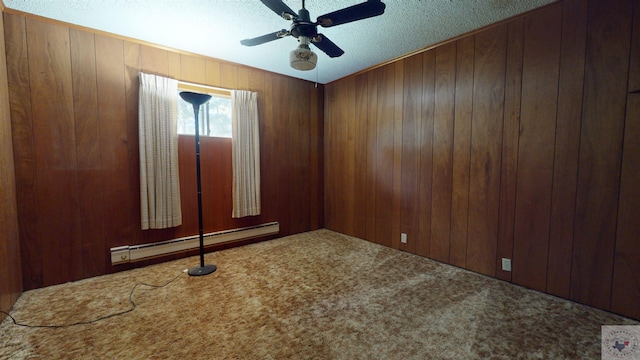 carpeted empty room with ceiling fan, wood walls, baseboard heating, and a textured ceiling