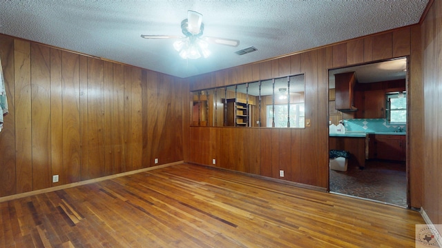 unfurnished room with ceiling fan, wooden walls, a textured ceiling, and wood-type flooring