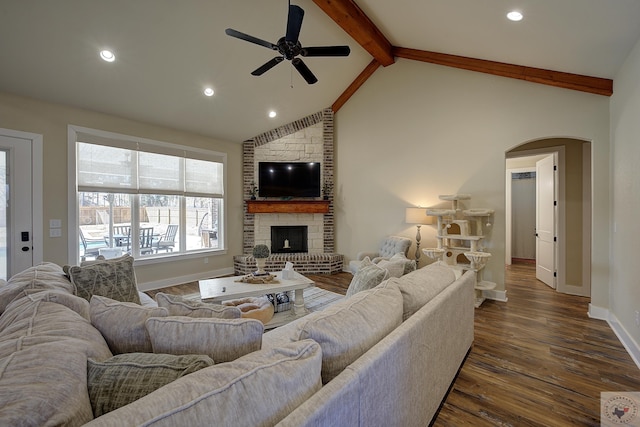 living room featuring dark hardwood / wood-style floors, ceiling fan, a fireplace, and vaulted ceiling with beams