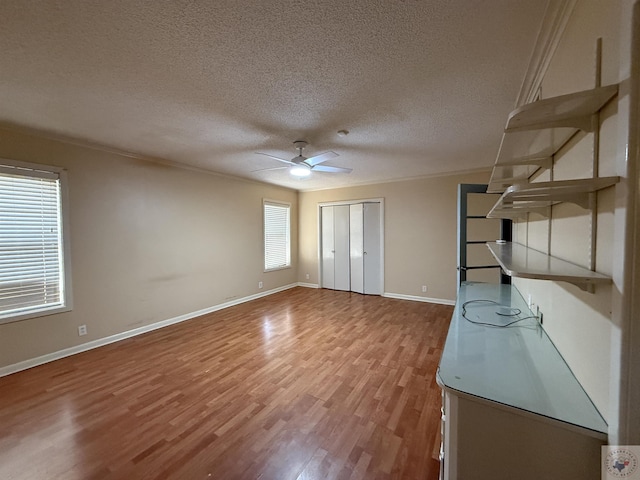 unfurnished bedroom featuring a textured ceiling, wood-type flooring, a closet, ornamental molding, and ceiling fan