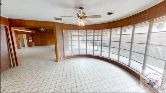 empty room with ceiling fan, a textured ceiling, and wooden walls