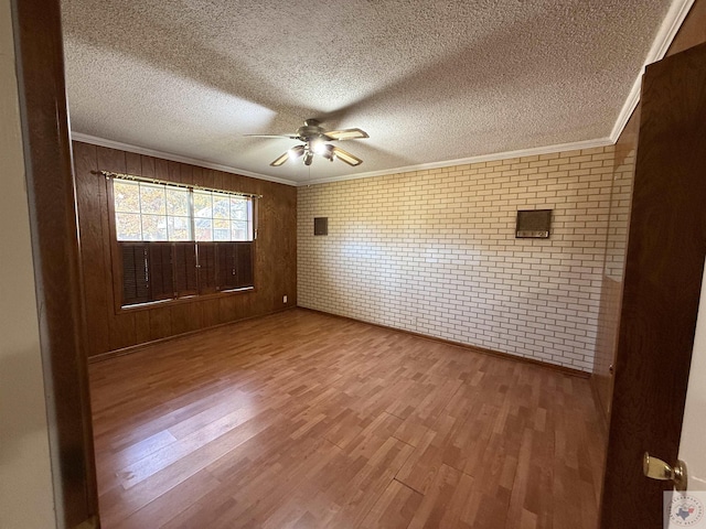 spare room with crown molding, a textured ceiling, wood-type flooring, brick wall, and ceiling fan