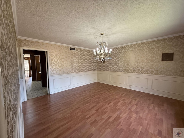 spare room with hardwood / wood-style flooring, ornamental molding, an inviting chandelier, and a textured ceiling