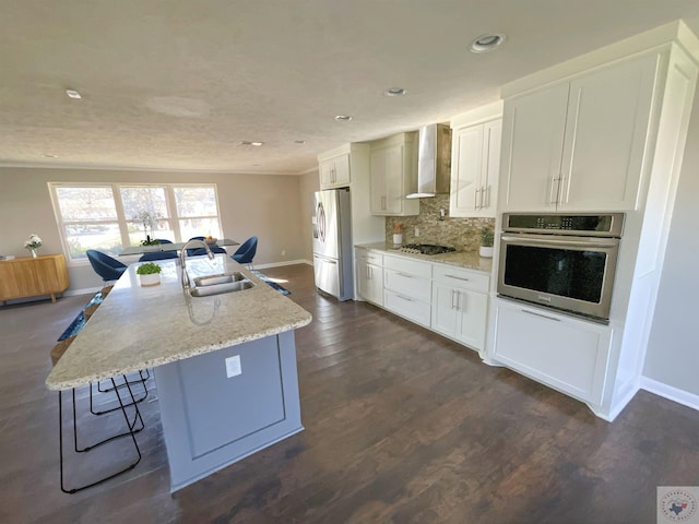 kitchen featuring wall chimney exhaust hood, sink, white cabinets, a center island with sink, and stainless steel appliances