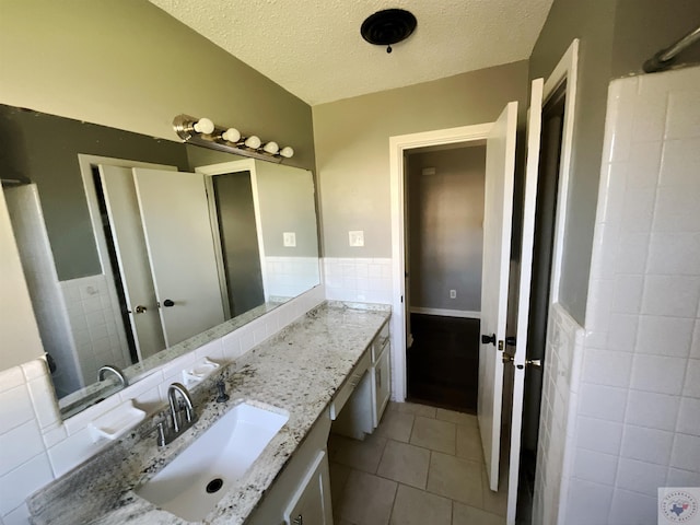 bathroom with vanity, vaulted ceiling, a textured ceiling, and tile patterned flooring