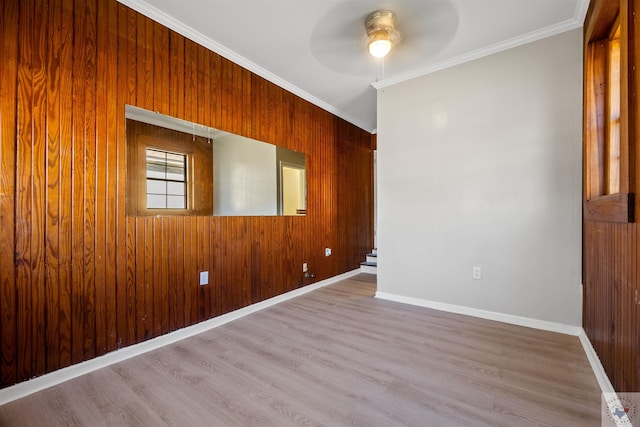 spare room with light wood-type flooring, ceiling fan, wood walls, and crown molding