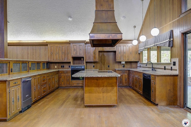 kitchen with custom exhaust hood, a sink, brown cabinets, black appliances, and a kitchen island