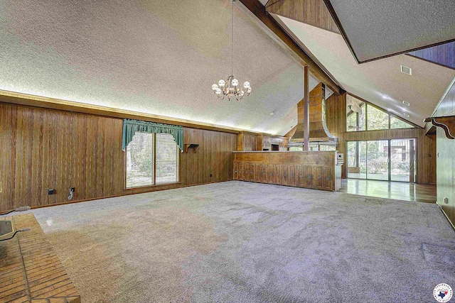 unfurnished living room with a notable chandelier, a textured ceiling, beam ceiling, carpet floors, and wood walls