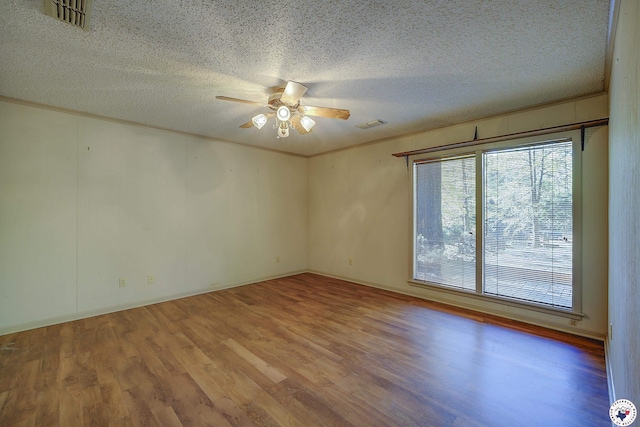 empty room with a textured ceiling, a ceiling fan, crown molding, visible vents, and wood finished floors