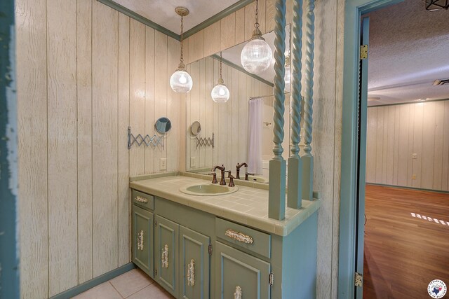 bathroom with a textured ceiling, wooden walls, tile patterned flooring, and vanity
