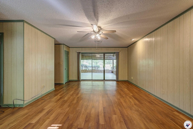 unfurnished room featuring crown molding, ceiling fan, a textured ceiling, wood finished floors, and wood walls