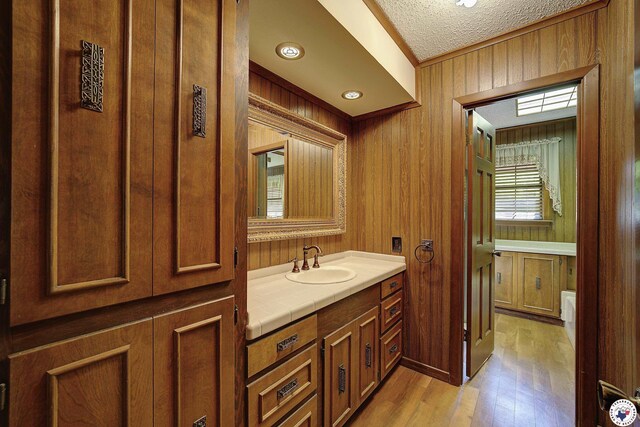 bathroom with wood walls, wood finished floors, vanity, and a textured ceiling