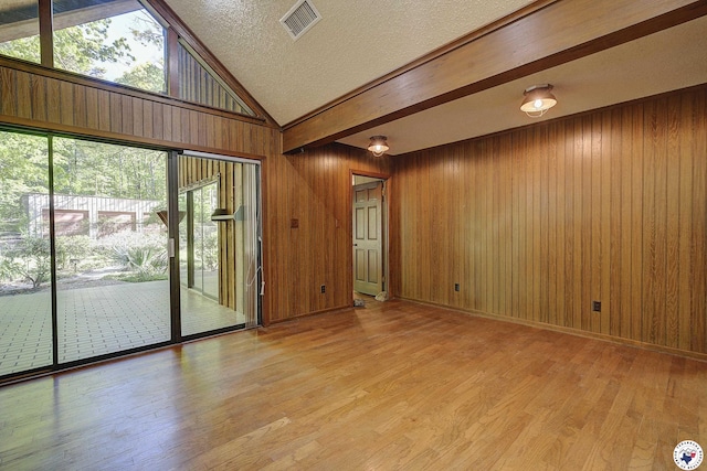 spare room with wood walls, visible vents, vaulted ceiling, and light wood-style flooring