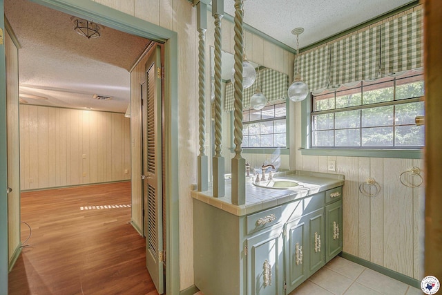interior space featuring wood walls, tile countertops, a textured ceiling, and a sink
