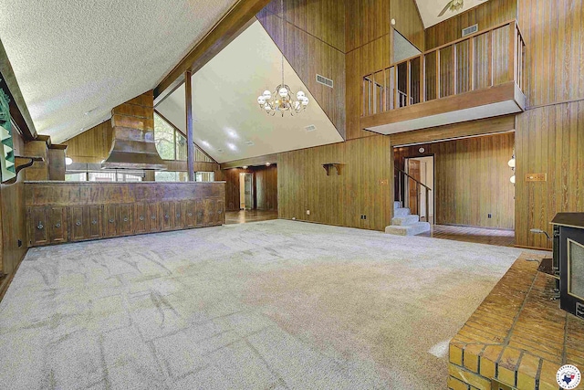 unfurnished living room with stairway, a notable chandelier, wooden walls, and visible vents