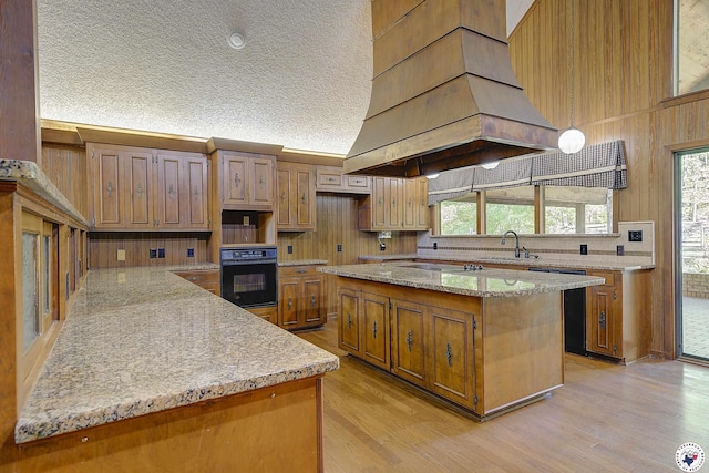 kitchen featuring custom exhaust hood, backsplash, black appliances, light wood finished floors, and a sink