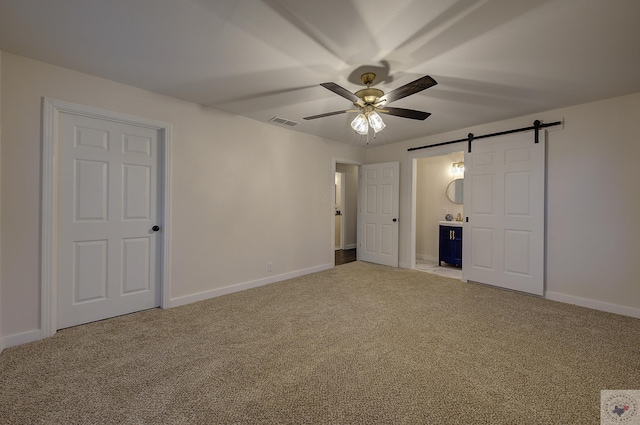 unfurnished bedroom featuring ensuite bathroom, a barn door, carpet flooring, and ceiling fan