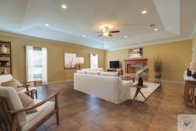 living room featuring ceiling fan, a brick fireplace, and a tray ceiling